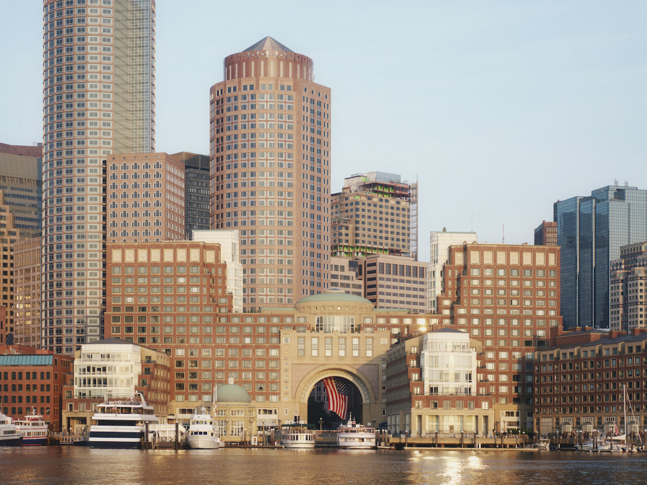 The image shows a waterfront city skyline with high-rise buildings and boats docked in the harbor, with reflections in the water.