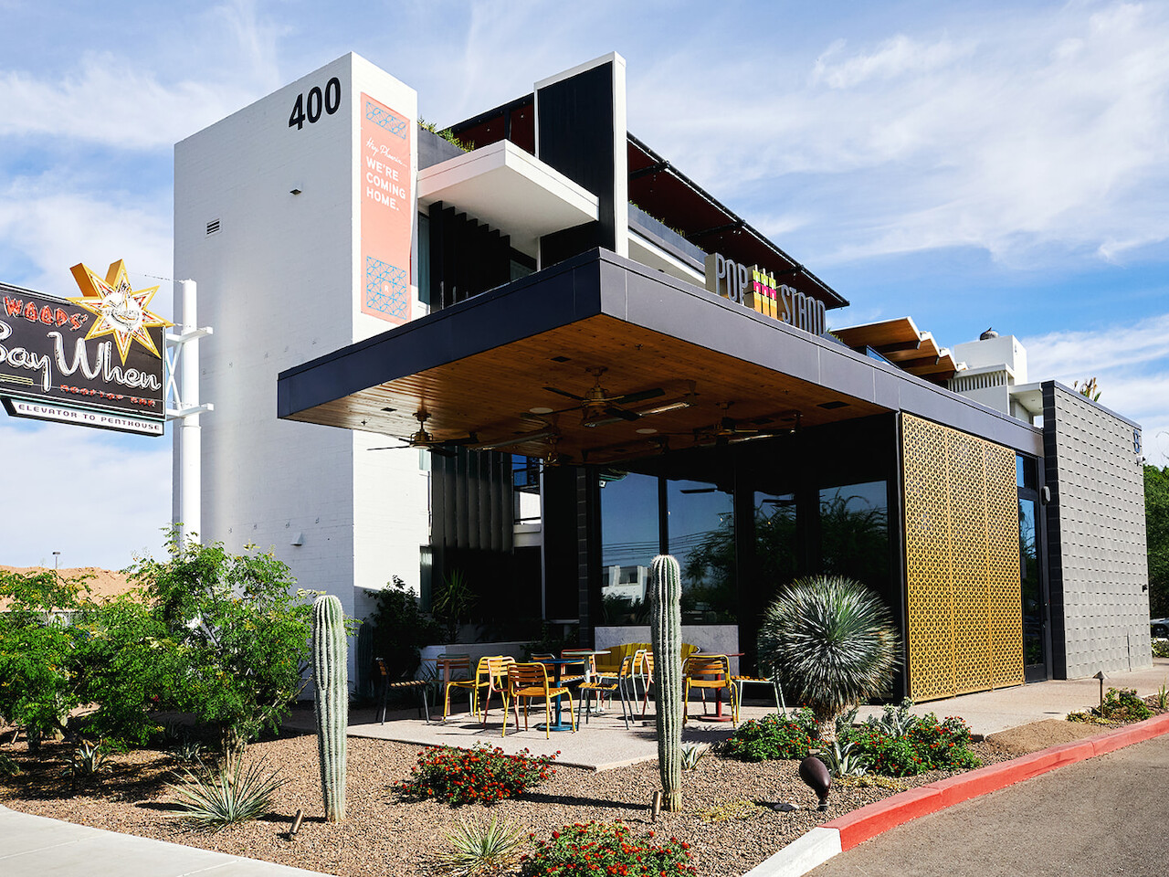 A modern building with a sign that says &amp;quot;Stay Wild&amp;quot; at the entrance, located at 400, with outdoor seating and desert landscaping.