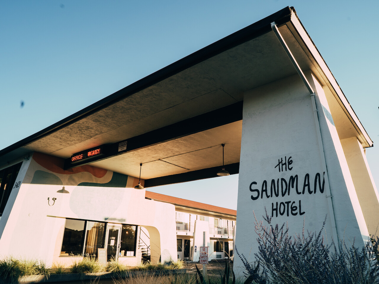 The image shows the exterior of The Sandman Hotel, featuring a large overhang, visible signage, and part of the hotel building in the background.