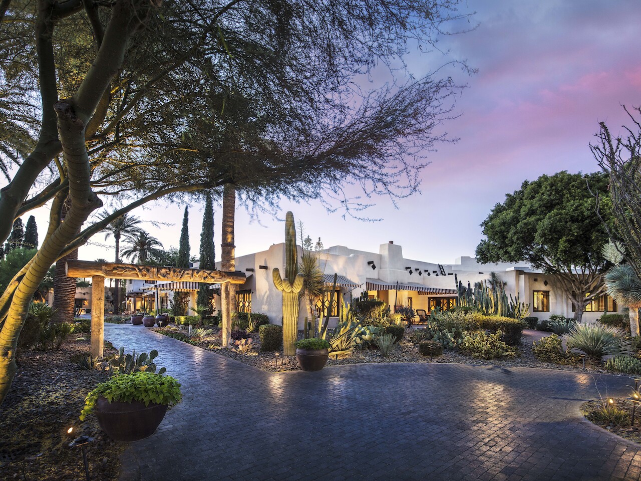 A serene desert landscape featuring a southwestern-style building surrounded by cacti and desert plants at twilight, with soft lighting illuminating the scene.