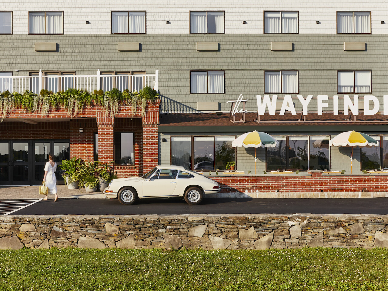 Una mujer camina hacia un edificio con un cartel que dice "The Wayfinder". Frente a él hay un coche clásico aparcado.