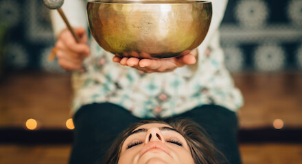 A person lies down as another holds a singing bowl above them, creating a serene and meditative atmosphere.