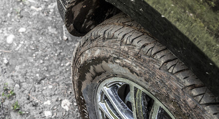 The image shows a close-up of a muddy tire and wheel of a vehicle on a dirt road.