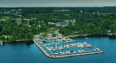 The image shows an aerial view of a marina with boats docked, surrounded by lush greenery and residential buildings in the background.