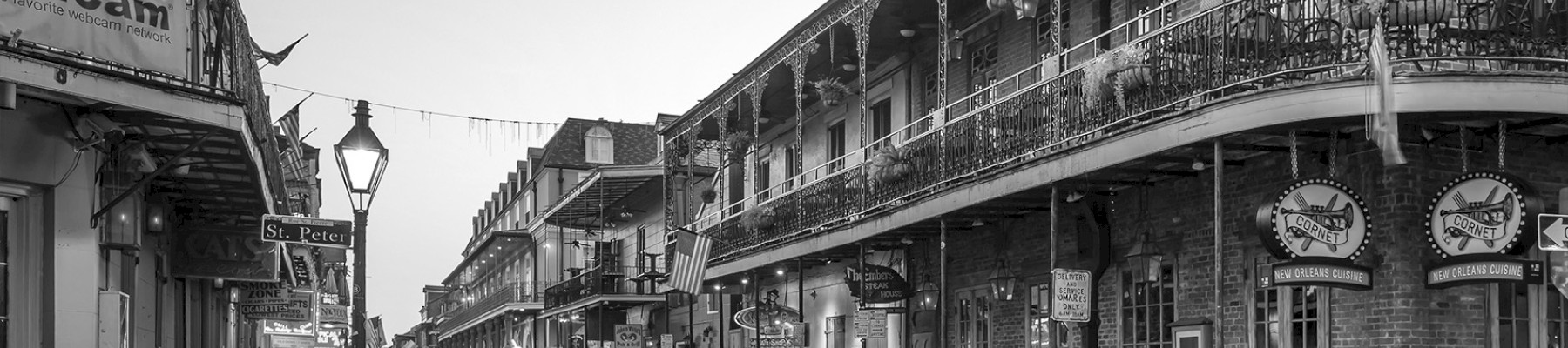 A black and white photo of a quiet street in a historic district with brick buildings and ornate iron balconies, likely early morning or evening.