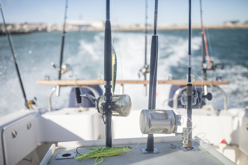 A close-up view of several fishing rods mounted on the back of a boat, moving through the water with the shoreline visible in the background.