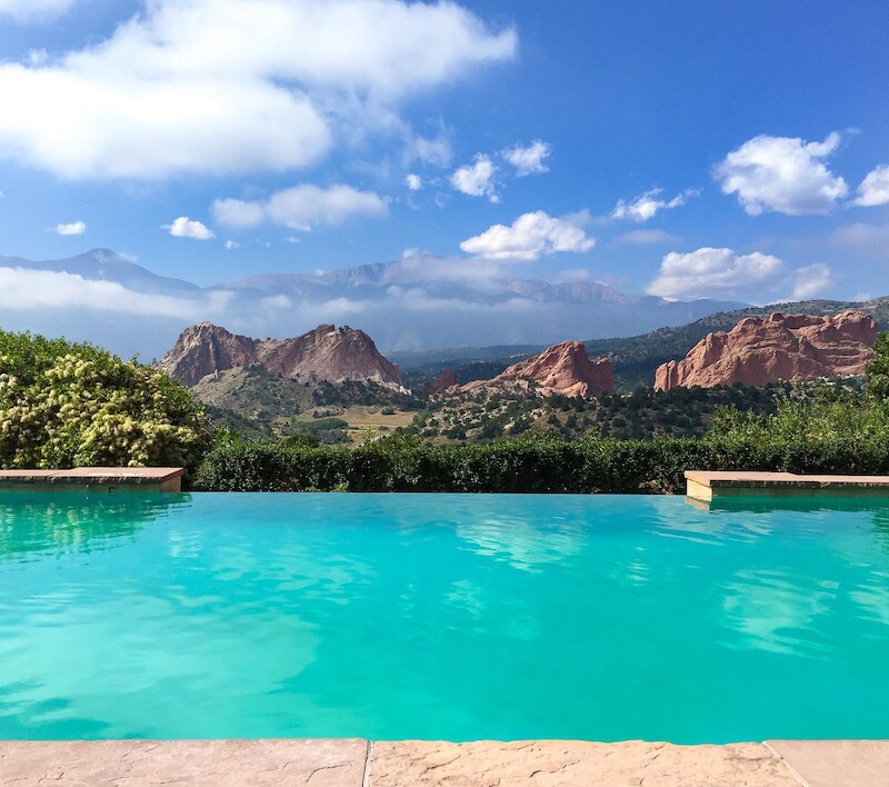 An infinity pool overlooks a scenic landscape featuring rocky hills and a blue sky with scattered clouds, creating a serene and picturesque view.