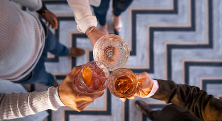 A top-down view of three people clinking their drinks together in a celebratory toast over a patterned floor, capturing their camaraderie.